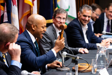 The chair of the Chesapeake Executive Council, seated at a long table, raises a gavel while his fellow council members, smiling and seated alongside him, look on.
